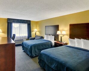 A hotel room with two beds, a desk, a chair, a lamp, and a window with curtains.