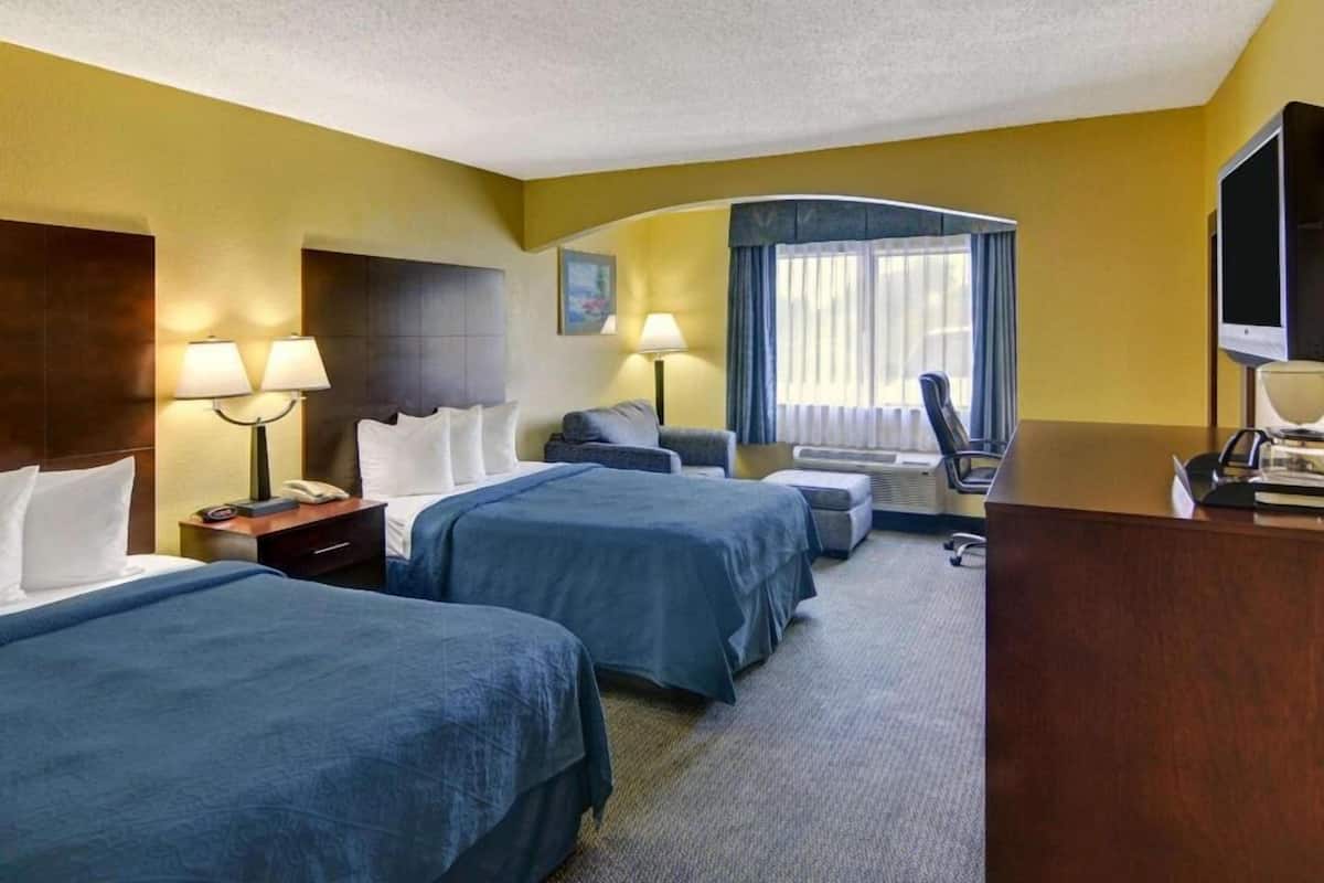 A hotel room with two beds, a desk, a chair, a TV, and a window with curtains.