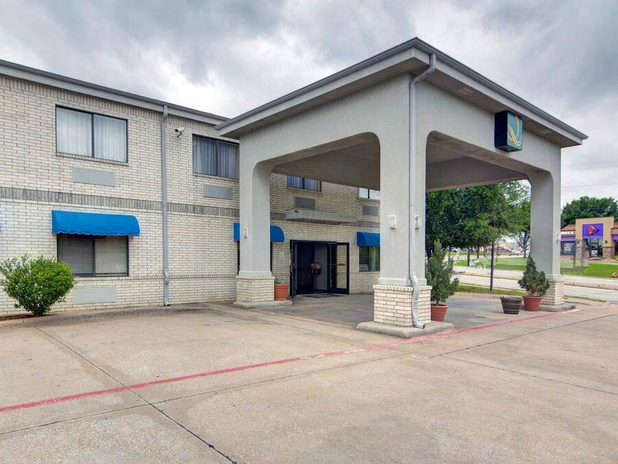 A motel with a covered entrance, brick facade, and potted plants.