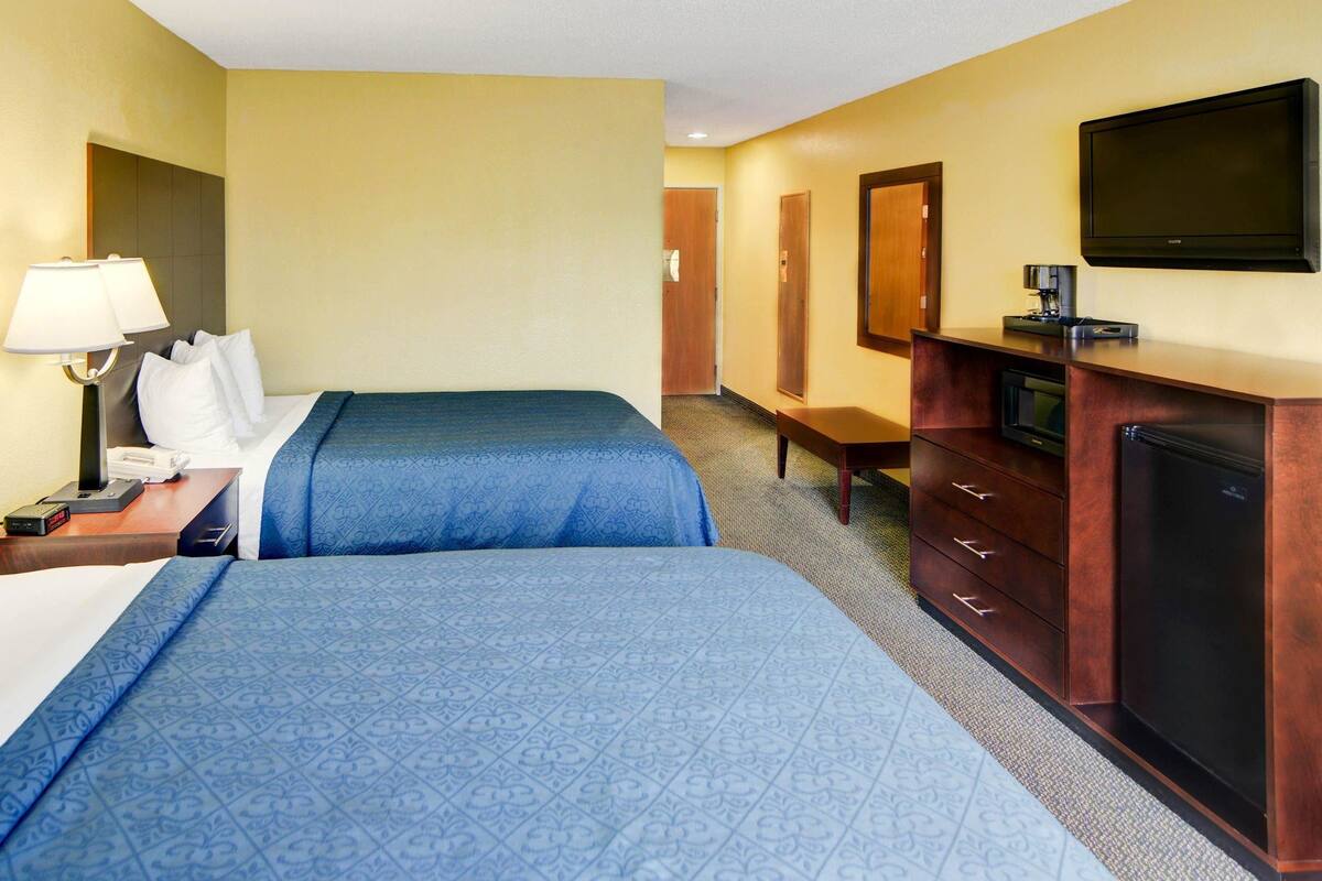A hotel room with two beds, a desk with a lamp, a television, and a minibar.