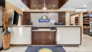 A reception area with a reception desk, a large logo of Days Inn by Wyndham, a chandelier, and a wall-mounted television.
