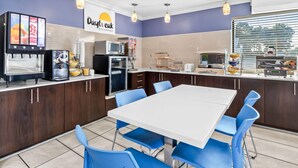 A breakfast area with a white table and blue chairs, a coffee machine, a microwave, and a sign reading "Daybreak Breakfast".