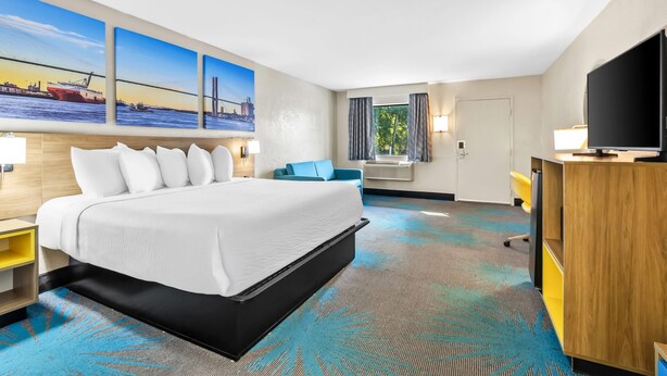 A hotel room with a large bed, a TV, a desk, and a window with curtains.