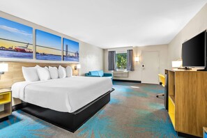 A hotel room with a large bed, a TV, a desk, and a window with curtains. - Days Inn by Wyndham Goose Creek (Goose Creek)