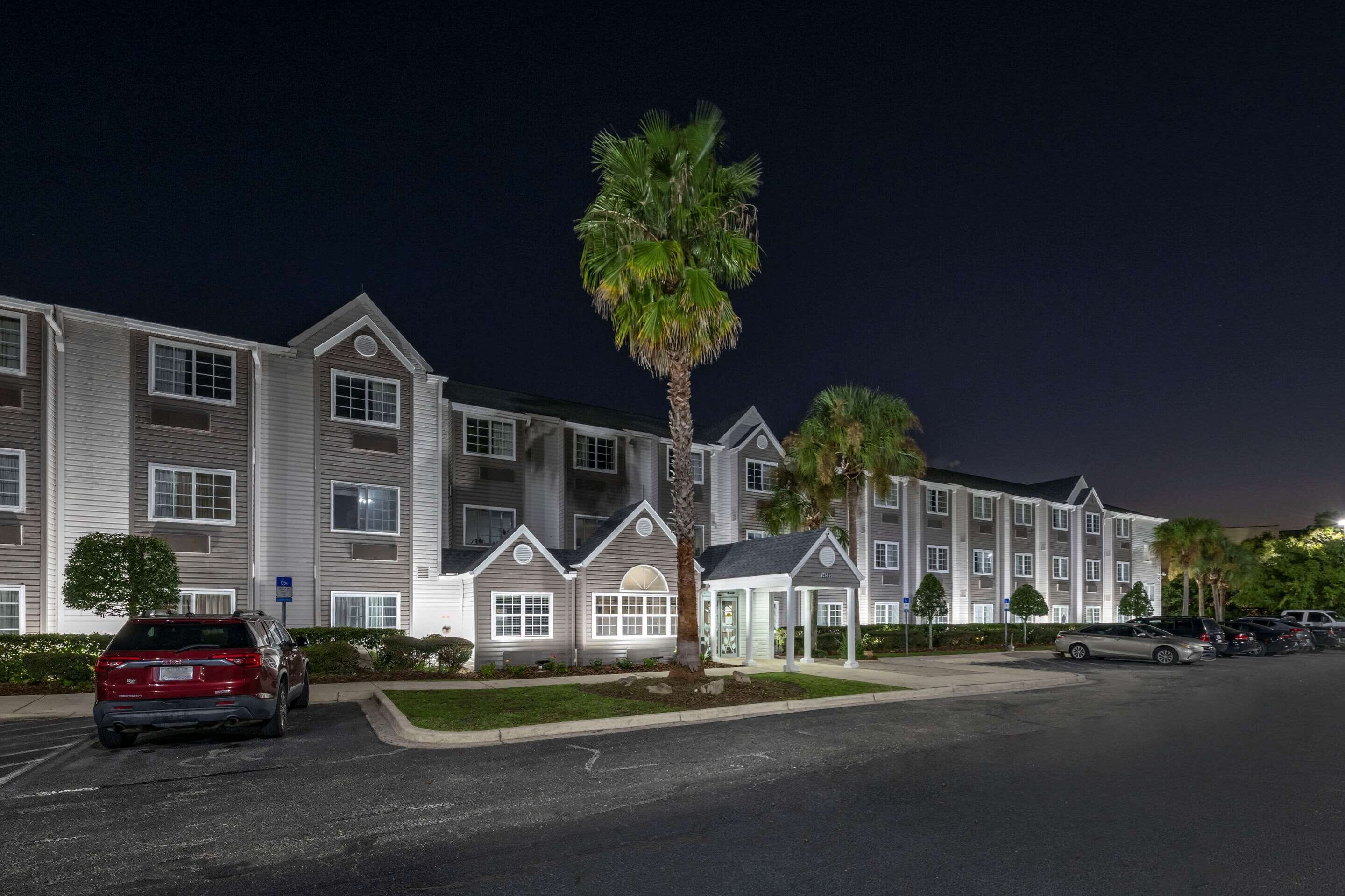 A multi-story hotel with a parking lot and a palm tree in the foreground.