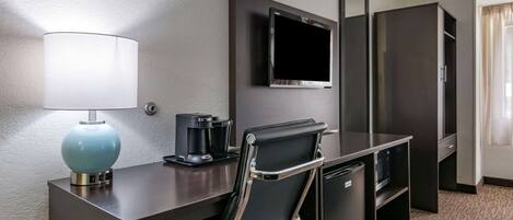 Una habitación de hotel con escritorio, silla, televisor, cafetera y minibar.