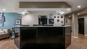 A reception area with a black reception desk, a sofa, and a coffee table. There are framed pictures on the wall and a door with a sign above it. - Sleep Inn Jacksonville Airport (Jacksonville)