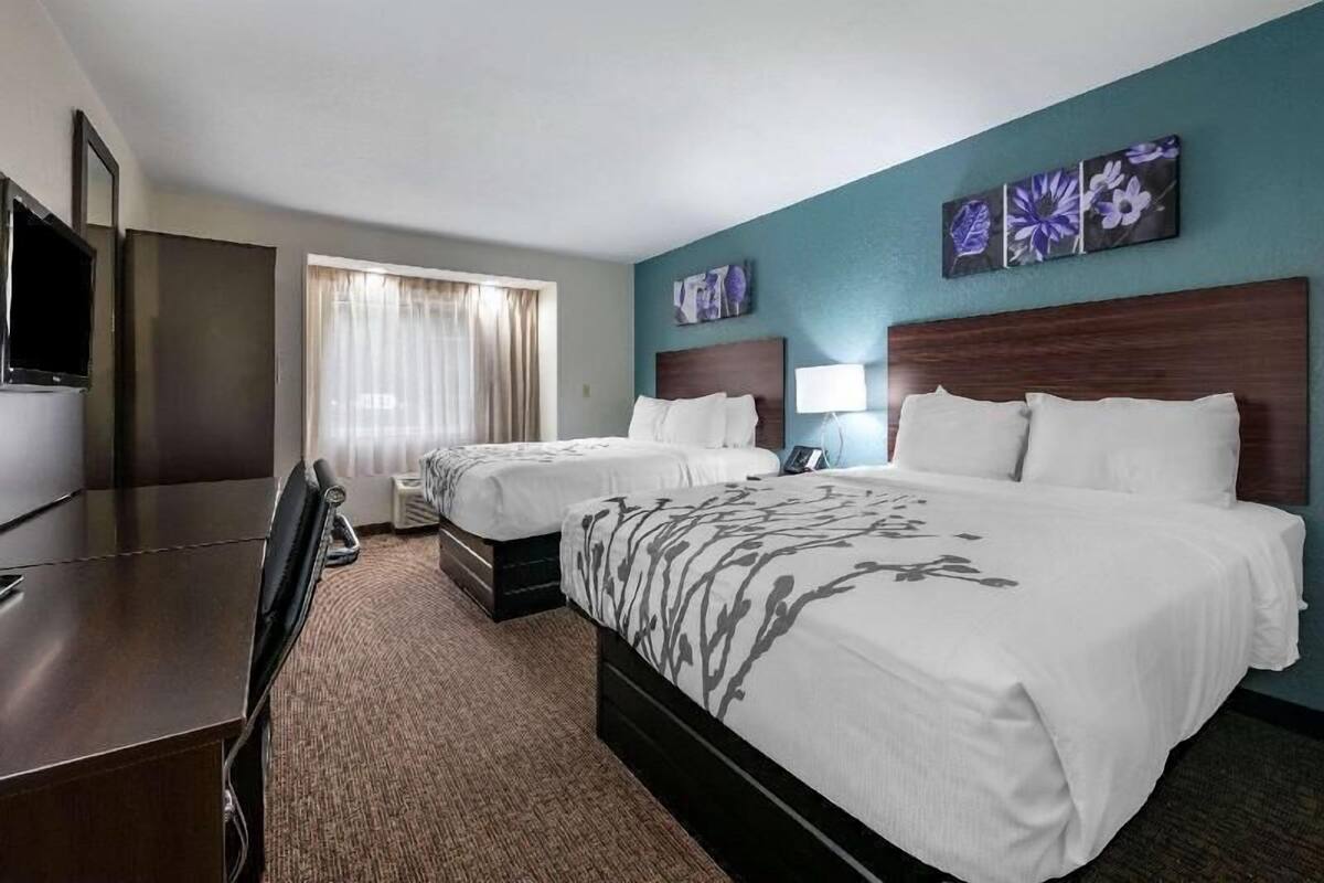 Une chambre d’hôtel avec deux lits, un bureau, une télévision et une fenêtre avec des rideaux.