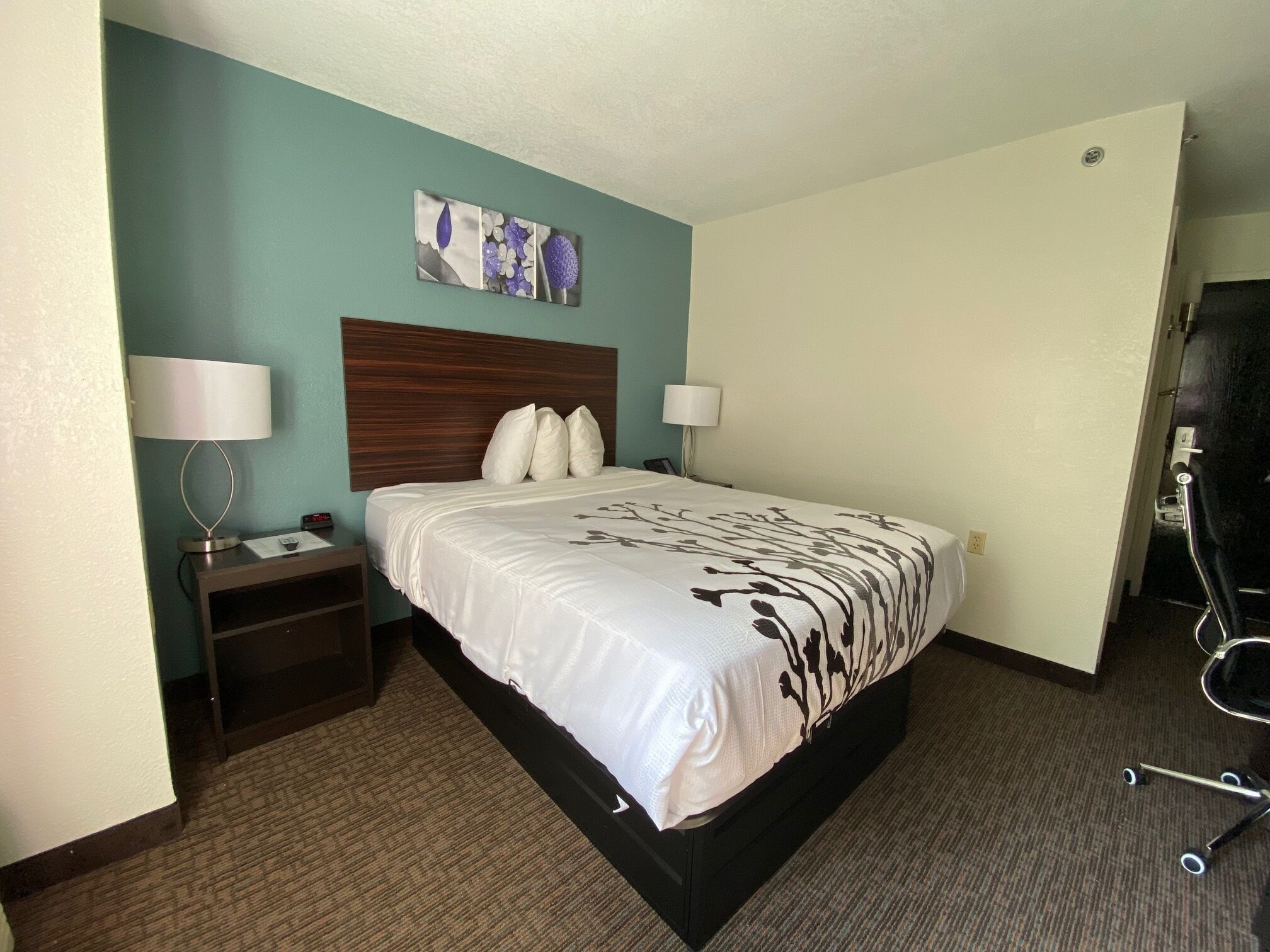 A hotel room with a large bed, two bedside tables with lamps, a headboard, and a wall-mounted artwork.