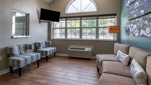A living room with a high ceiling, a large arched window, a flat-screen TV, patterned sofas, and a wall-mounted air conditioner. - Sleep Inn Jacksonville Airport (Jacksonville)