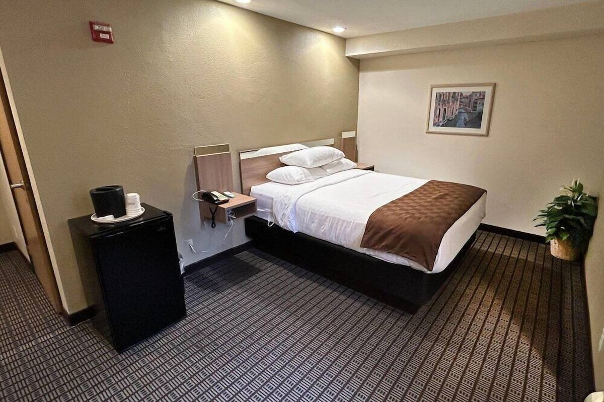 Ett hotellrum med en säng, ett nattduksbord och ett litet svart kylskåp.