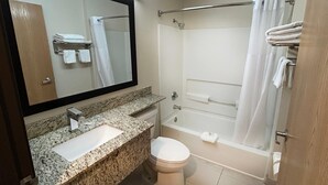 Ein Badezimmer mit Granitwaschtisch, Toilette, Badewanne mit Duschvorhang und großem Spiegel.