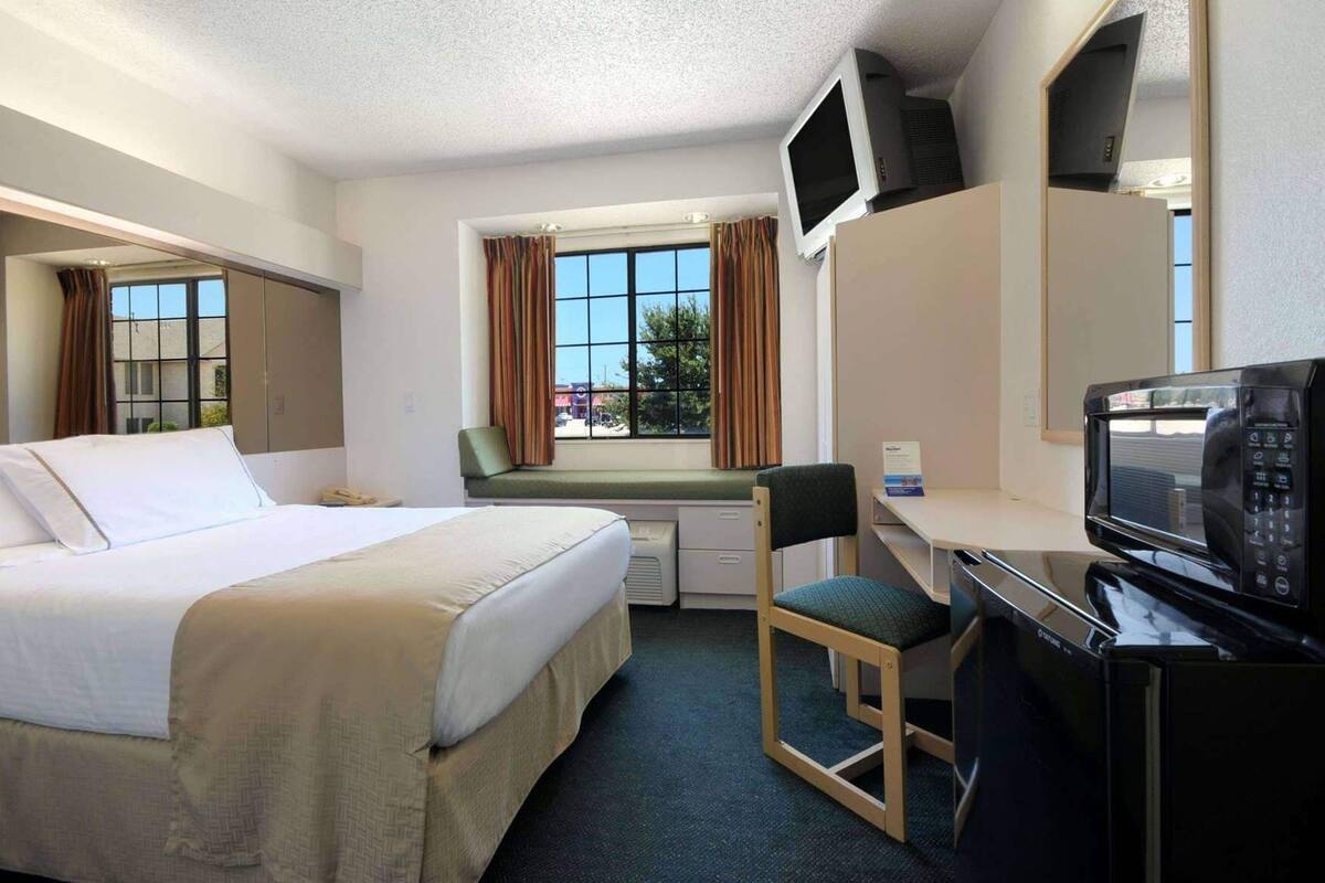 Ett hotellrum med en säng, ett skrivbord, en stol, en tv och ett fönster med gardiner.