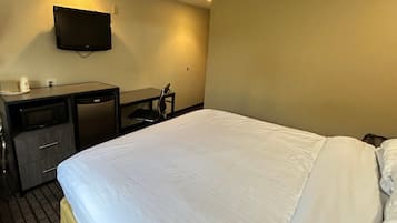 Quarto de hotel com cama, escrivaninha, cadeira, televisão na parede e uma pequena mesa com xícara e pires.