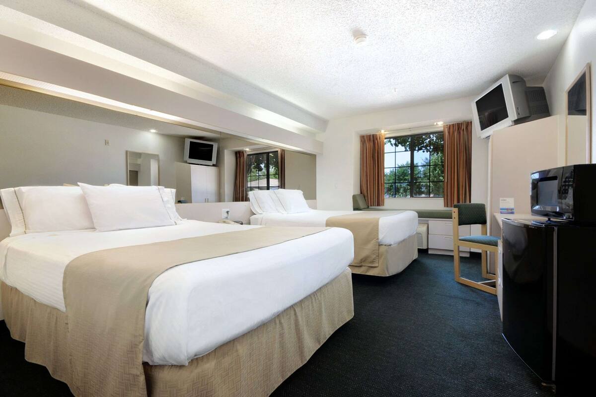 Ett hotellrum med två sängar, ett skrivbord, en TV och ett fönster med gardiner.