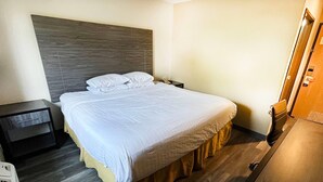 Ein ordentlich bezogenes Bett mit weißen Leinen, ein Holzkopfstück und ein Nachttisch mit einer Lampe.