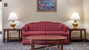 A room with a red sofa, two side tables with lamps, a framed picture on the wall, and a carpeted floor. - Econo Lodge Saint Stephen (St. Stephen)