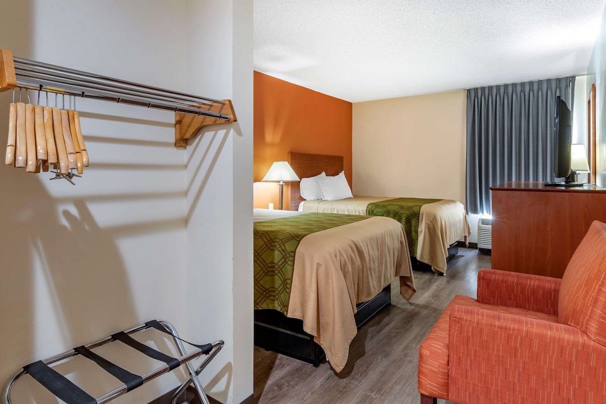 Une chambre d’hôtel avec deux lits, une chaise en bois, un bureau avec un téléviseur à écran plat et une fenêtre avec des rideaux.