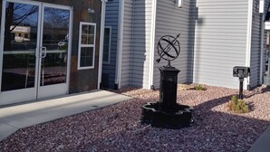 A modern building with large windows and a small garden area with a decorative sculpture. - Days Inn & Suites by Wyndham Greeley (Greeley)