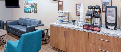 A hotel lobby with a seating area, a coffee station, and artwork on the walls.