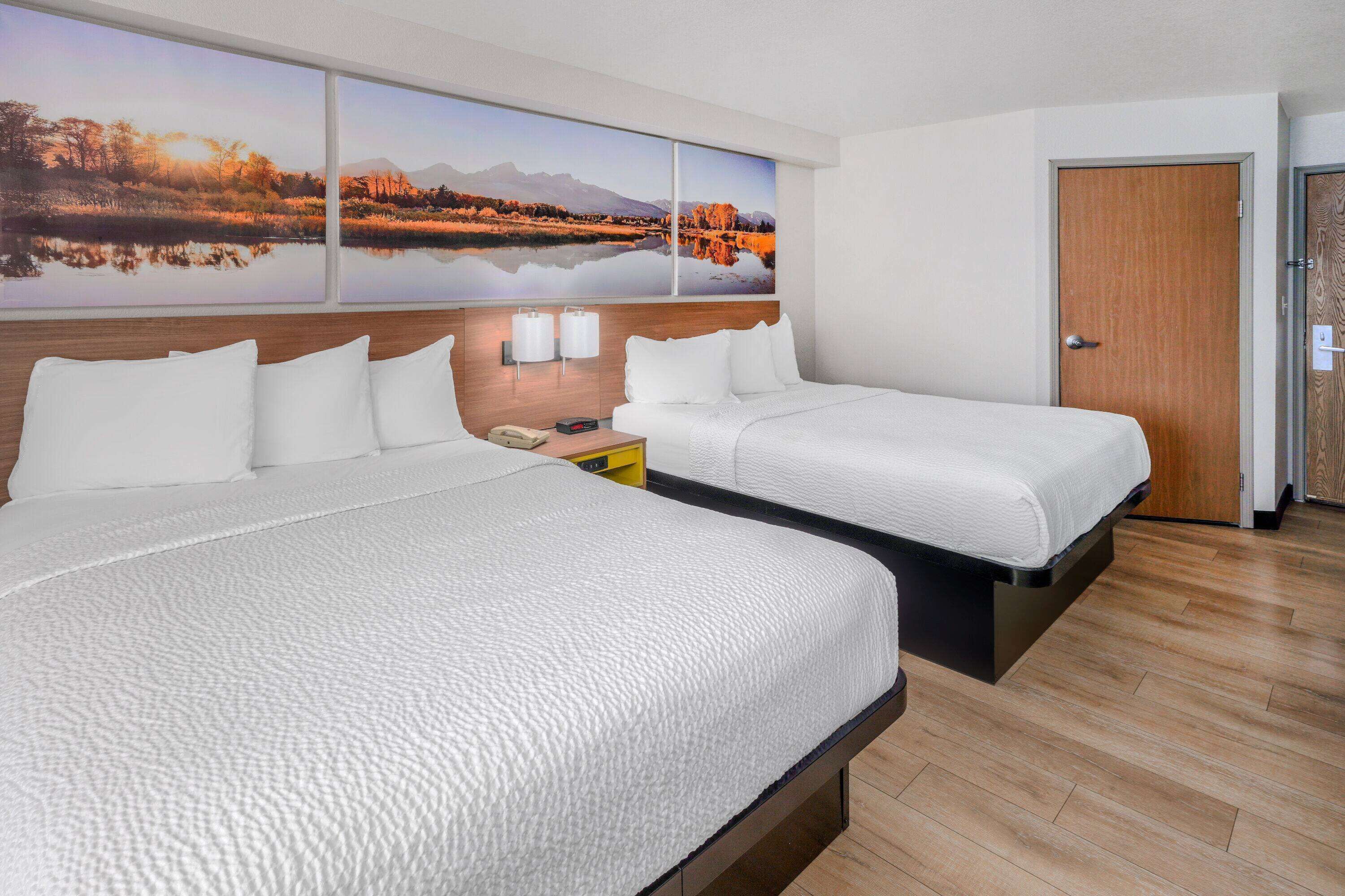 A hotel room with two beds, a wooden headboard, a large landscape painting, and a wooden door.
