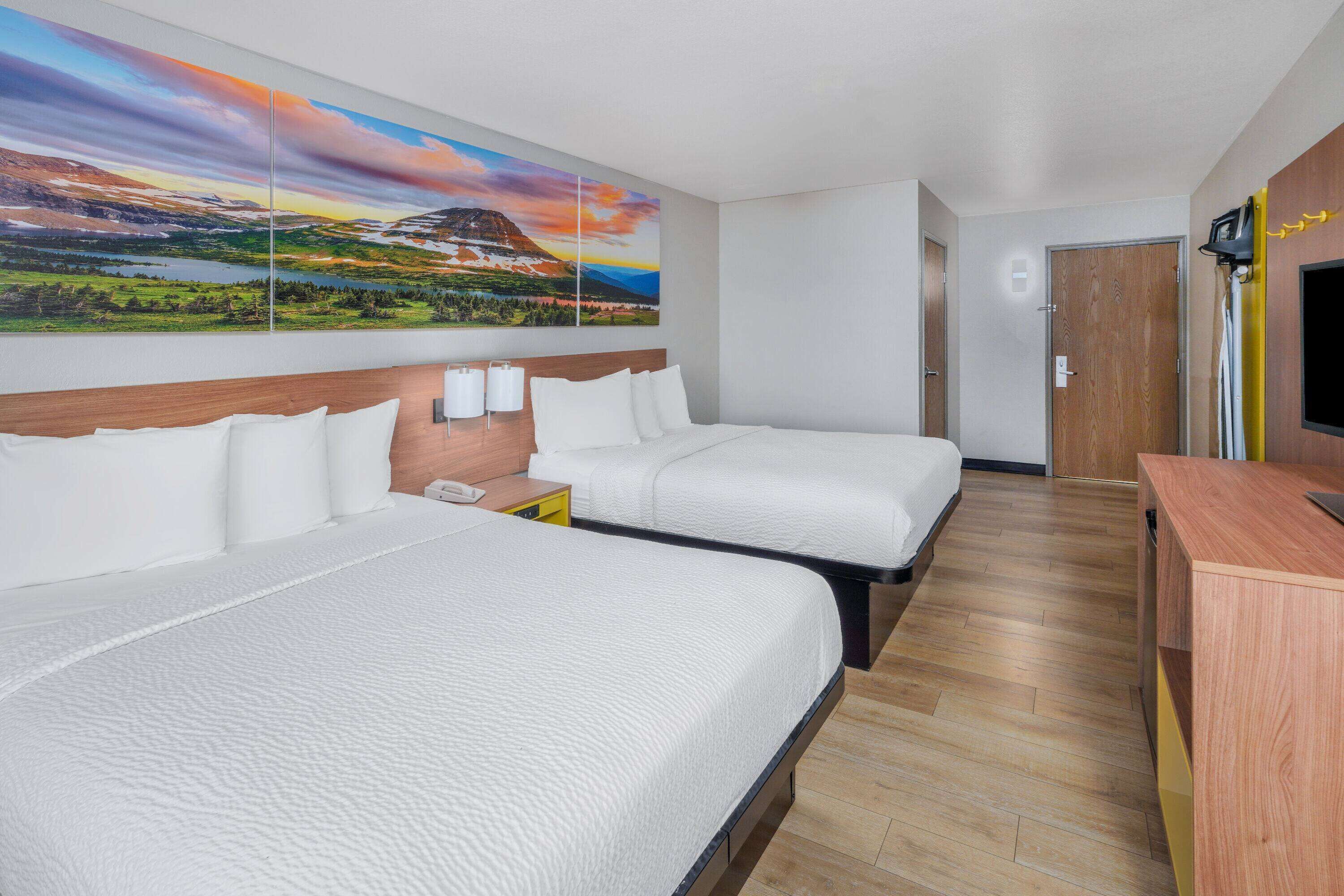 A hotel room with two beds, a wooden headboard, a large landscape painting, a wooden desk, and a television.