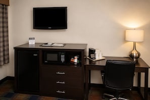 Habitación de hotel con televisión de pantalla plana, minibar, escritorio con lámpara y una silla.