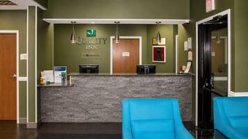 A hotel reception area with a reception desk, two blue chairs, and a wall-mounted sign for Quality Inn.