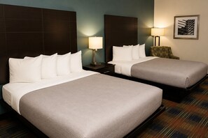 Habitación de hotel con dos camas, una mesita de noche, una lámpara y una silla.