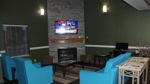 A living room with blue sofas, a fireplace, a television mounted above it, and a small table with magazines. - Quality Inn North Vernon near Hwy 50 (North Vernon)