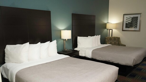 A hotel room with two beds, a nightstand with a lamp, a chair, and a framed picture on the wall. - Quality Inn North Vernon near Hwy 50 (North Vernon)