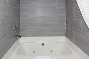 Un baño moderno con una bañera independiente, paredes de azulejos grises y una cortina de ducha blanca.