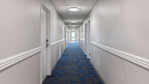 A long, narrow hotel corridor with white walls, a blue carpet, and white trim. - Microtel Inn by Wyndham Bowling Green (Bowling Green)