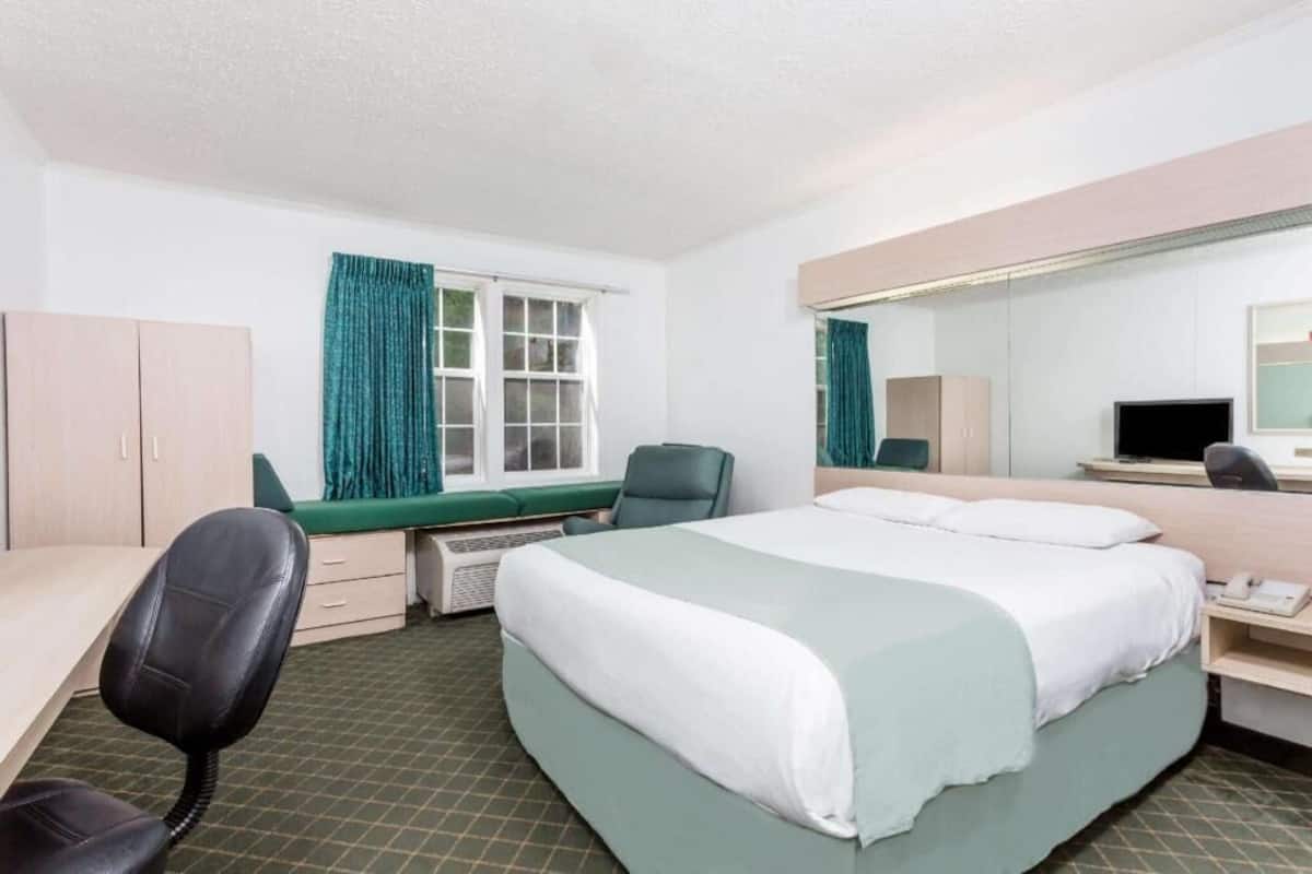 A hotel room with a bed, desk, chair, and a large mirror.