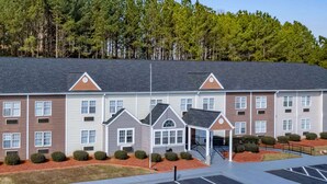A multi-story hotel with a central courtyard, parking lot, and a forested backdrop. - Microtel Inn by Wyndham Athens (Athens)