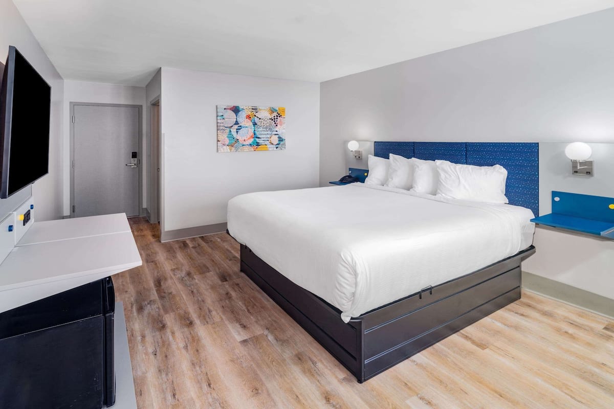 A modern hotel room with a large bed, a flat-screen TV, a desk, and a wall-mounted artwork.