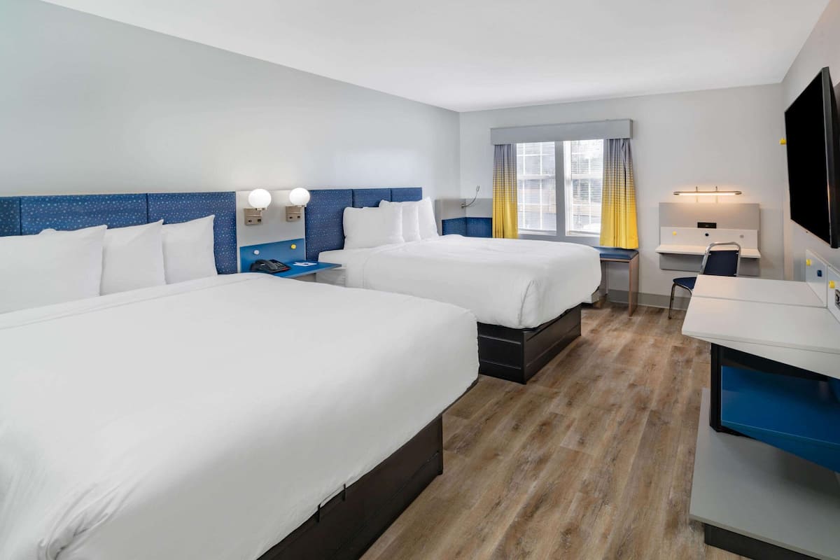 A hotel room with two beds, a desk, a chair, a TV, and a window with curtains.