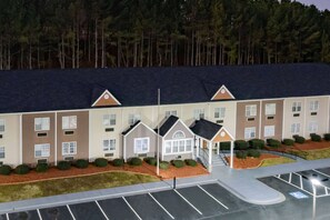 A multi-story hotel with a central entrance, parking lot, and a forested background. - Microtel Inn by Wyndham Athens (Athens)