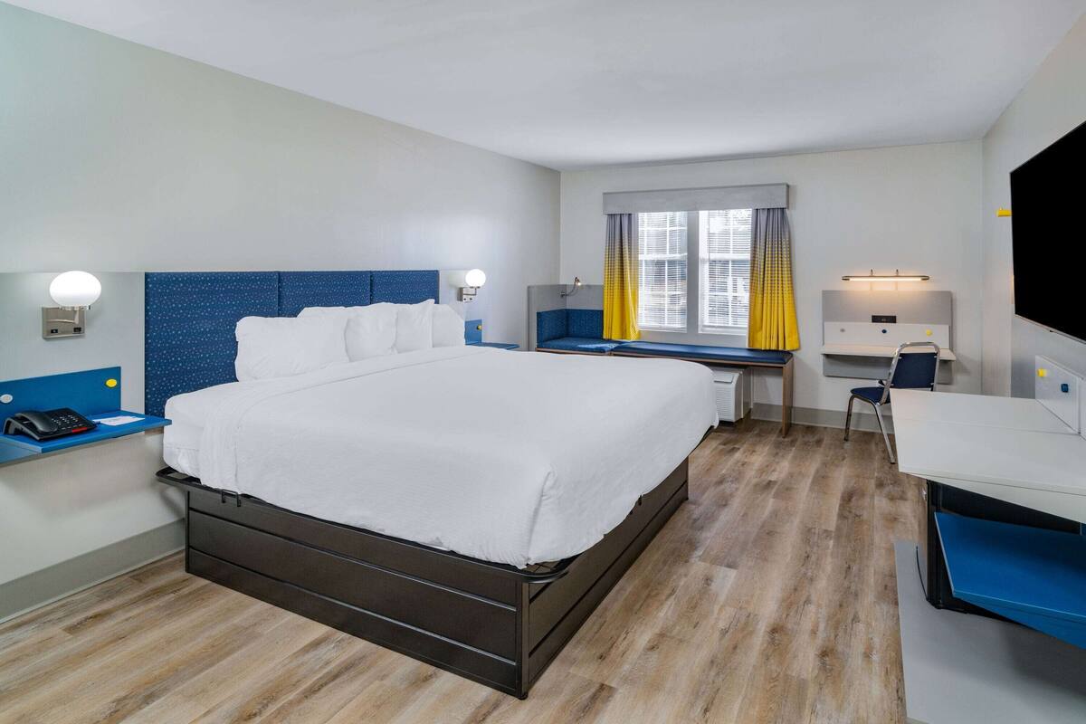 A hotel room with a large bed, a desk with a chair, a TV, and a window with curtains.