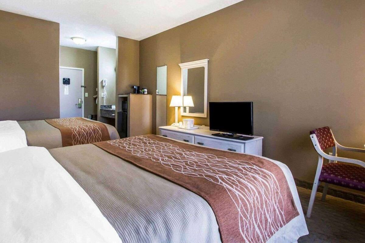 A hotel room with two beds, a television, a desk, a chair, and a mirror.