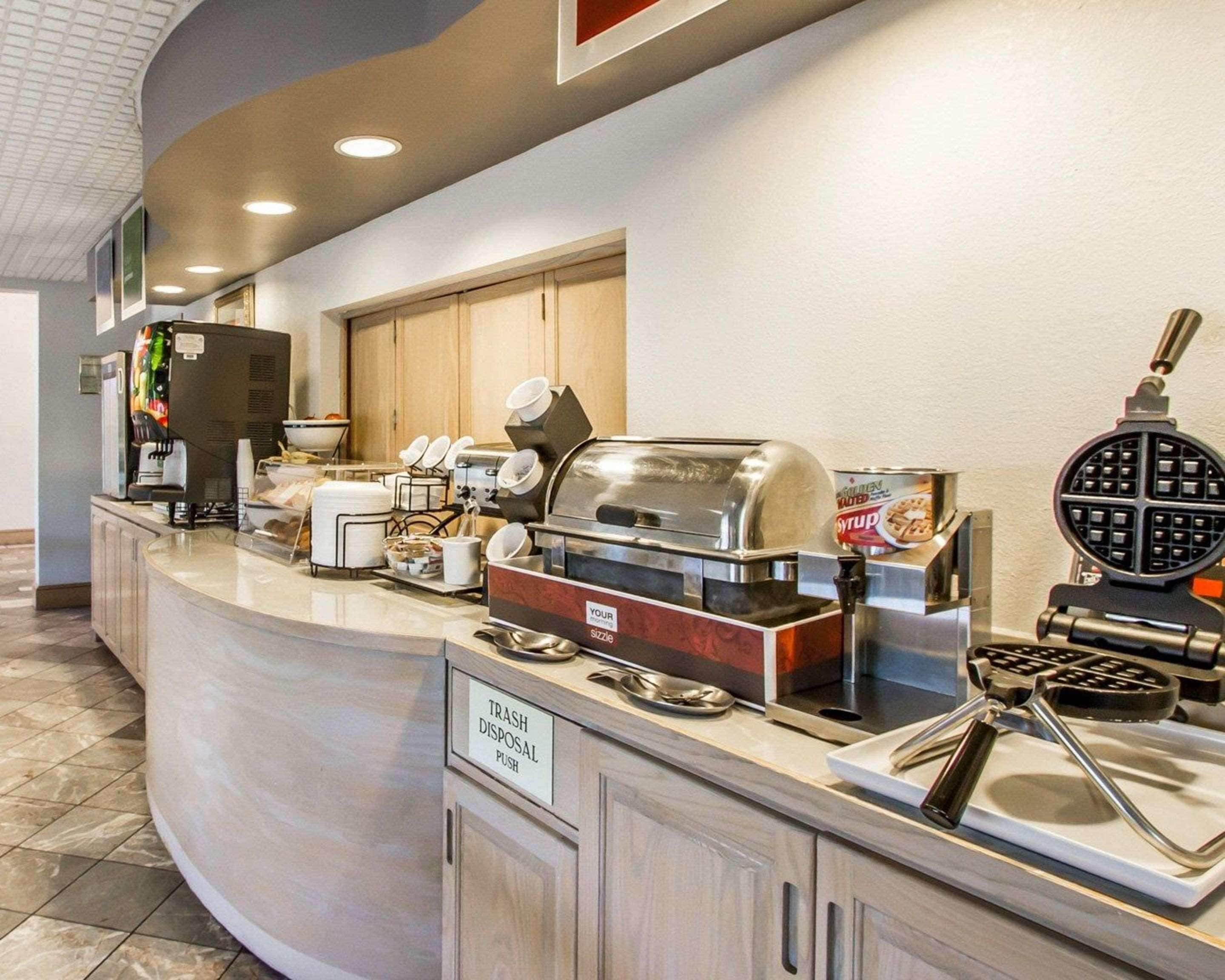 Un espace où l’on peut se servir soi-même pour le petit-déjeuner, comprenant une machine à café, un appareil à gaufres et une poubelle.