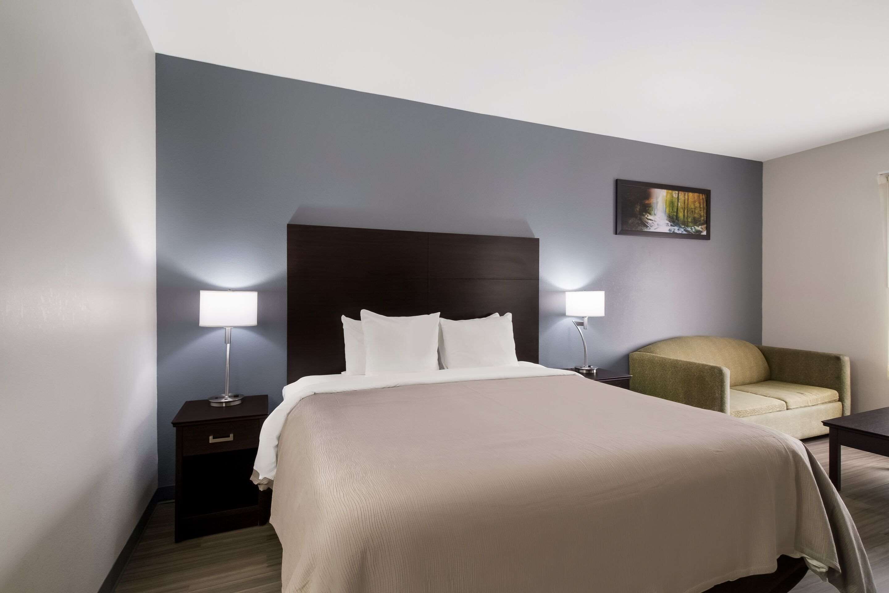 A hotel room with a large bed, two bedside lamps, a chair, a nightstand, and a painting on the wall.