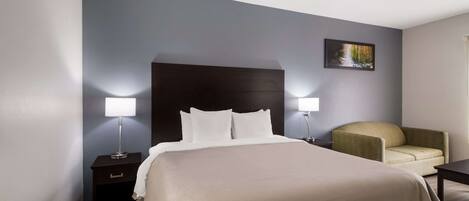 A hotel room with a large bed, two bedside lamps, a chair, a nightstand, and a painting on the wall.