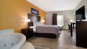 A hotel room with a large bed, a sitting area with a desk and chair, a television, and a bathtub. - Quality Inn Columbia I-65 (Columbia)