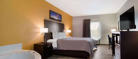 A hotel room with a large bed, a sitting area with a desk and chair, a television, and a bathtub.
