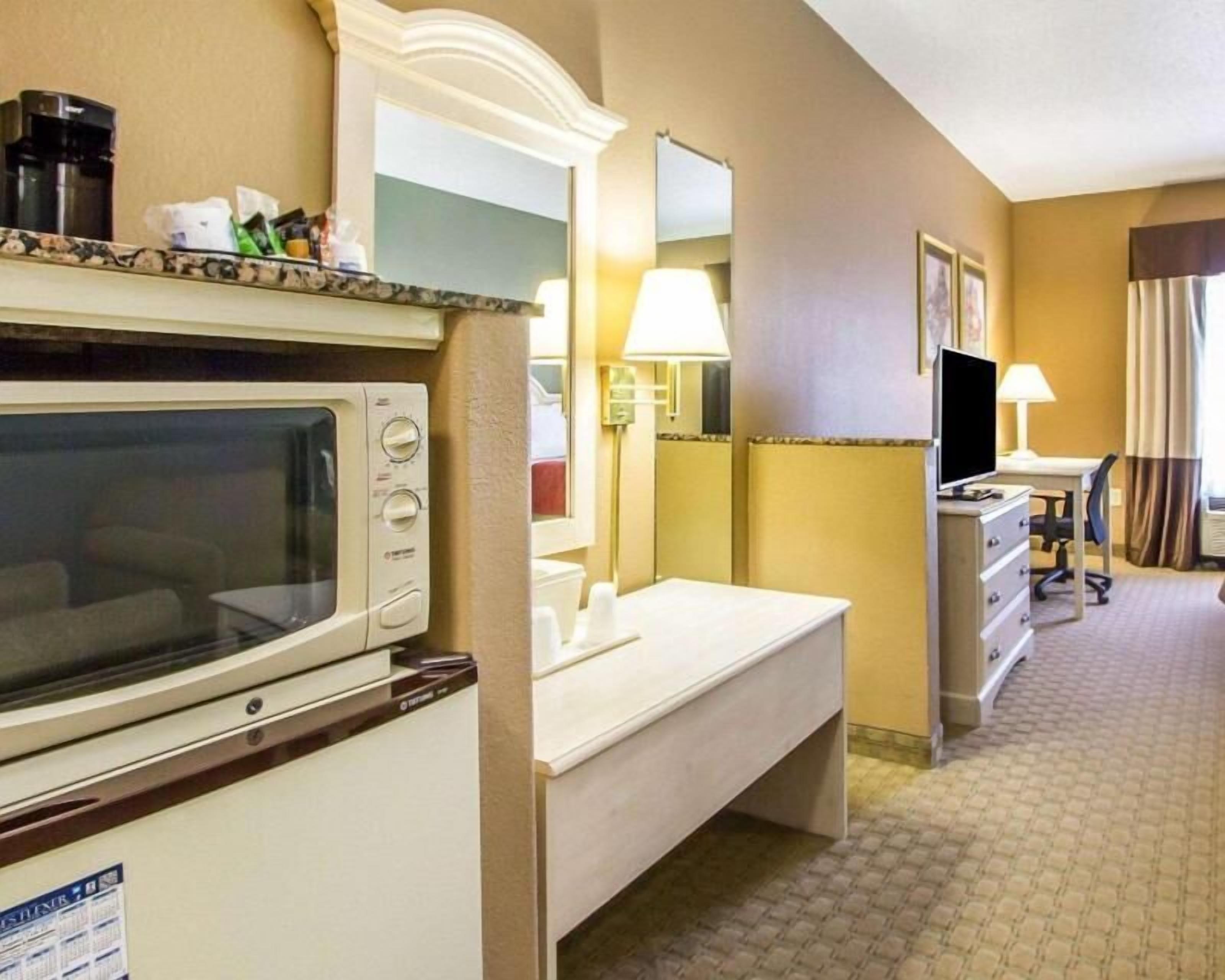 Habitación de hotel con microondas, tocador con espejo, escritorio y silla, y televisor.
