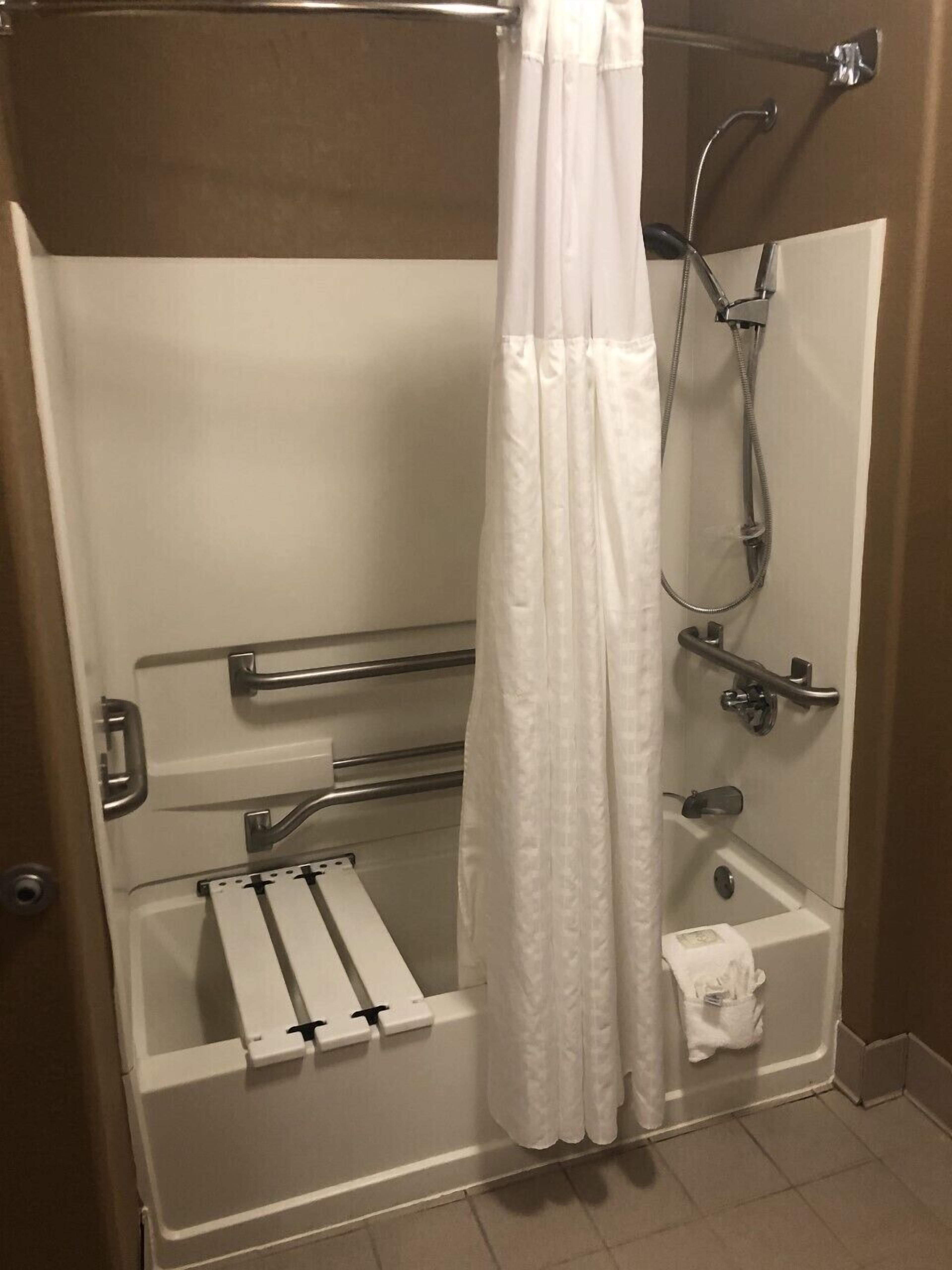 A shower stall with a white curtain, grab bars, a handheld showerhead, and a towel rack.
