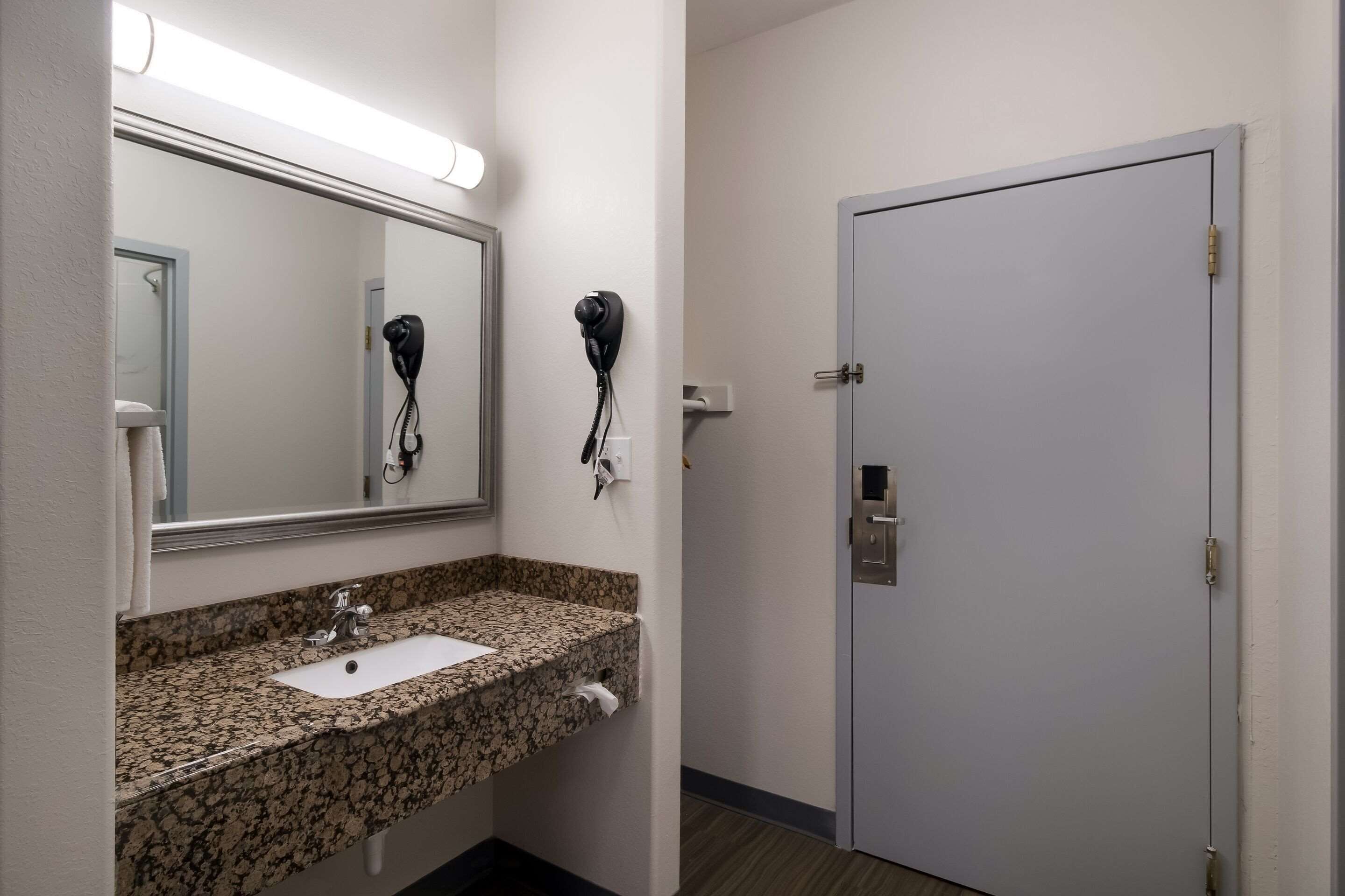 A bathroom with a granite countertop sink, a mirror, and two hair dryers mounted on the wall.
