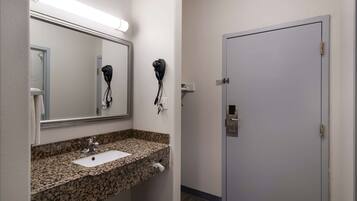 A bathroom with a granite countertop sink, a mirror, and two hair dryers mounted on the wall.