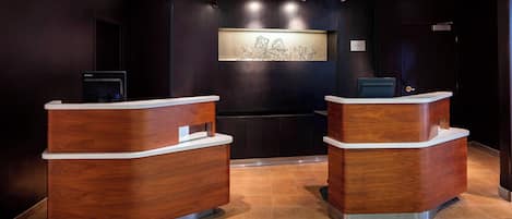 A reception area with two wooden reception desks, a wall-mounted artwork, and a digital screen.